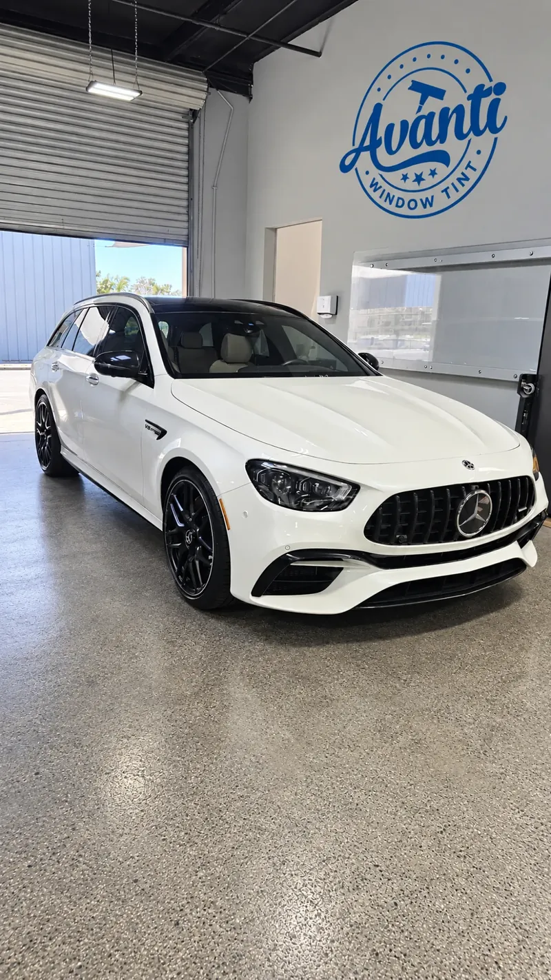 White Mercedes-AMG wagon with tinted windows inside the Avanti Window Tint shop, their badge on the wall
