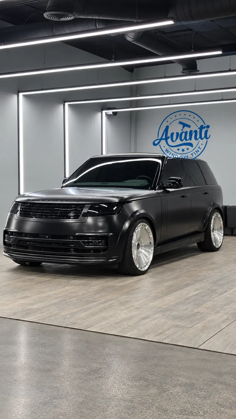 Matte black Range Rover with tinted windows in the lit bay at Avanti Window Tint